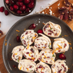 Pinterest image showing cranberry feta pinwheels on a plate surrounded by nuts and fruits.