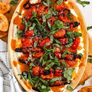 Creamy bruschetta dip topped with juicy tomatoes, fresh basil, and balsamic drizzle, served with toasted bread slices.