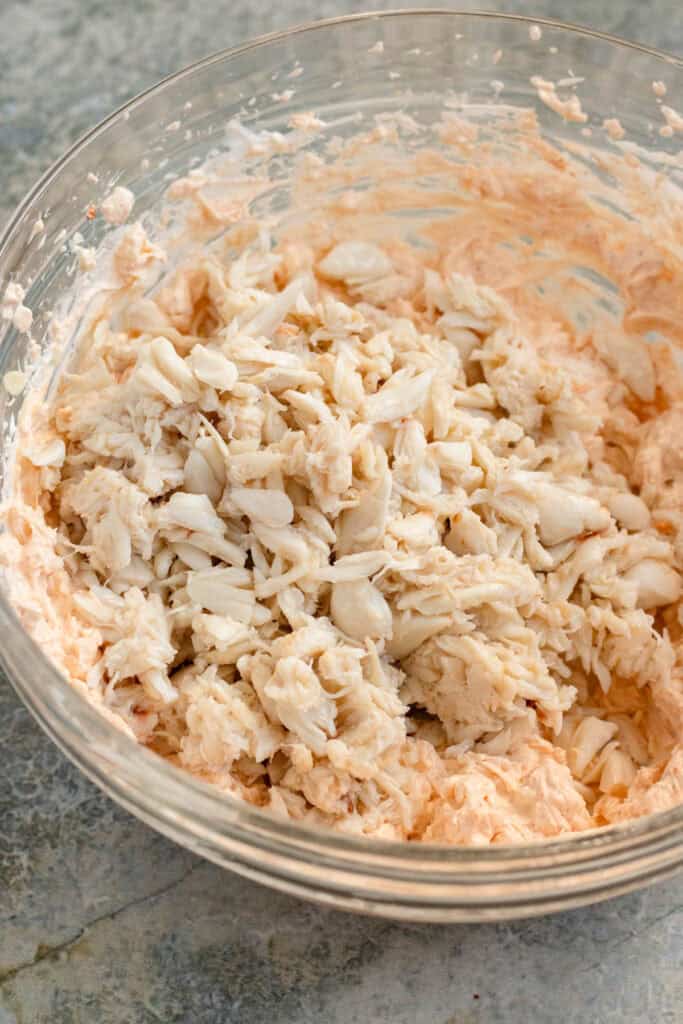 White cheddar, gruyère, and crab meat being folded into a creamy hot crab dip mixture.