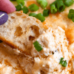 Pinterest image of a close-up shot of hand dipping a crostini in the creamy hot crab dip.