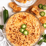 Pinterest image of a top-view shot of the Sausage Cheese Dip in a glass baking dish with whole and sliced jalapeños and toasted bread slices around it.