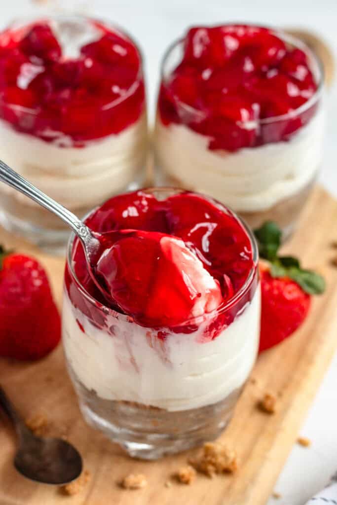 A spoon lifting a bite of strawberry-topped no-bake cheesecake cup.