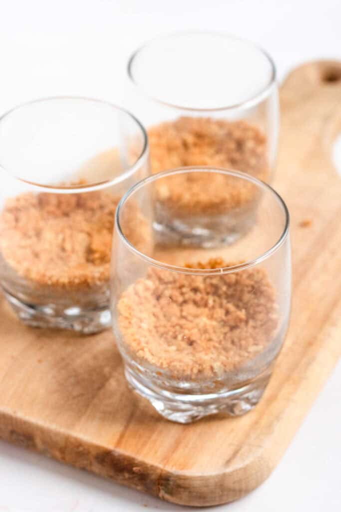 Pressing buttery graham cracker crumbs into the bottom of clear dessert cups.