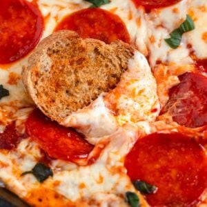 Close-up image of a cheesy Pizza Dip with melted mozzarella and fresh basil, featuring a crostini dipping into the gooey, melted center.
