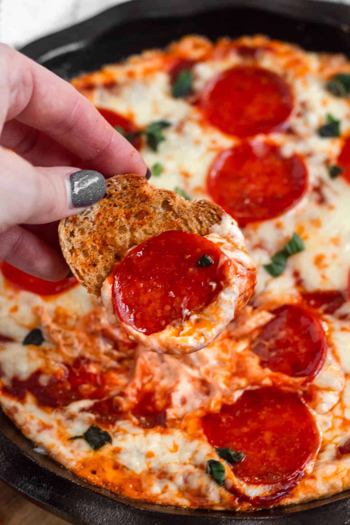 A hand taking a scoop of cheesy pizza dip with a piece of bread. 