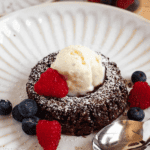 Pinterest image of the Molten Chocolate Lava Cake on a plate topped with vanilla ice cream and raspberry, with fresh berries and a spoon on the side.