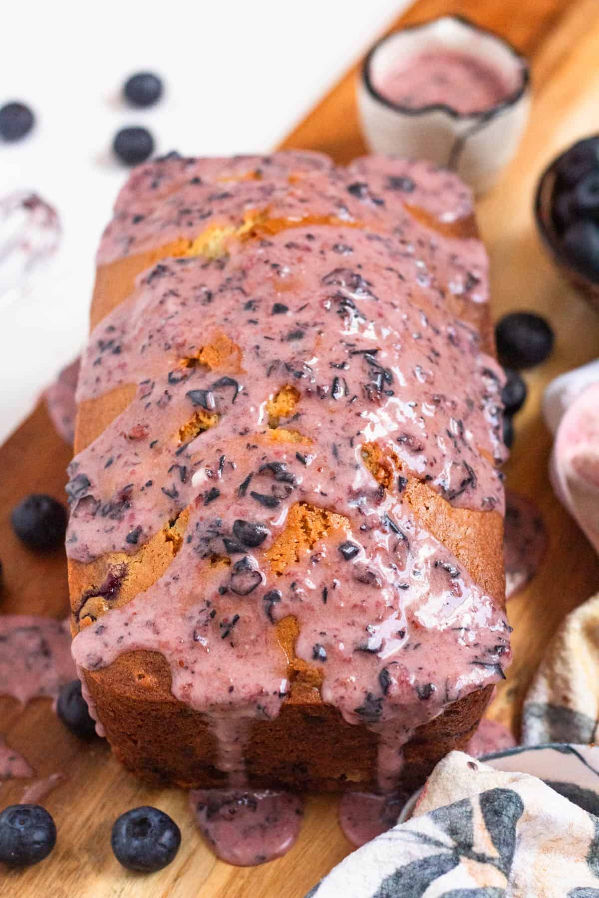 Blueberry Bread with a thick, glossy blueberry glaze dripping over the sides on a wooden board.