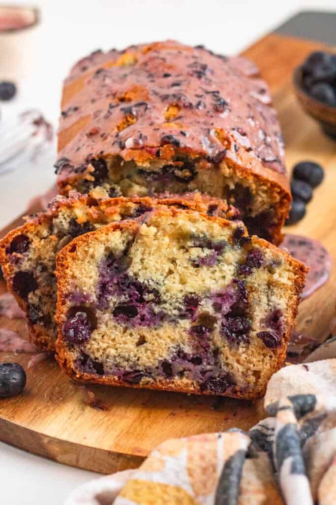Sliced Blueberry Bread with a soft, golden crumb and juicy berries, topped with a sweet blueberry glaze on a wooden board.
