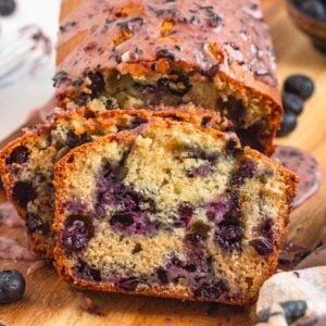 Sliced Blueberry Bread with a soft, golden crumb and juicy berries, topped with a sweet blueberry glaze on a wooden board.
