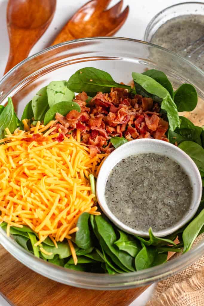 A large salad bowl filled with an untossed salad with cheese, bacon, and poppyseed dressing.