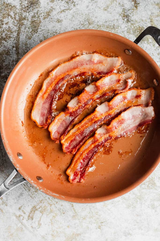 Bacon cooking in a pan until crispy and golden brown.