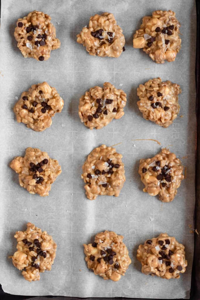 Avalanche cookies arranged on a parchment-lined baking sheet, topped with chocolate chips and flaky sea salt.