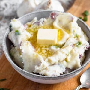 Close-up of a bowl of creamy red skin mashed potatoes topped with a melting pat of butter.