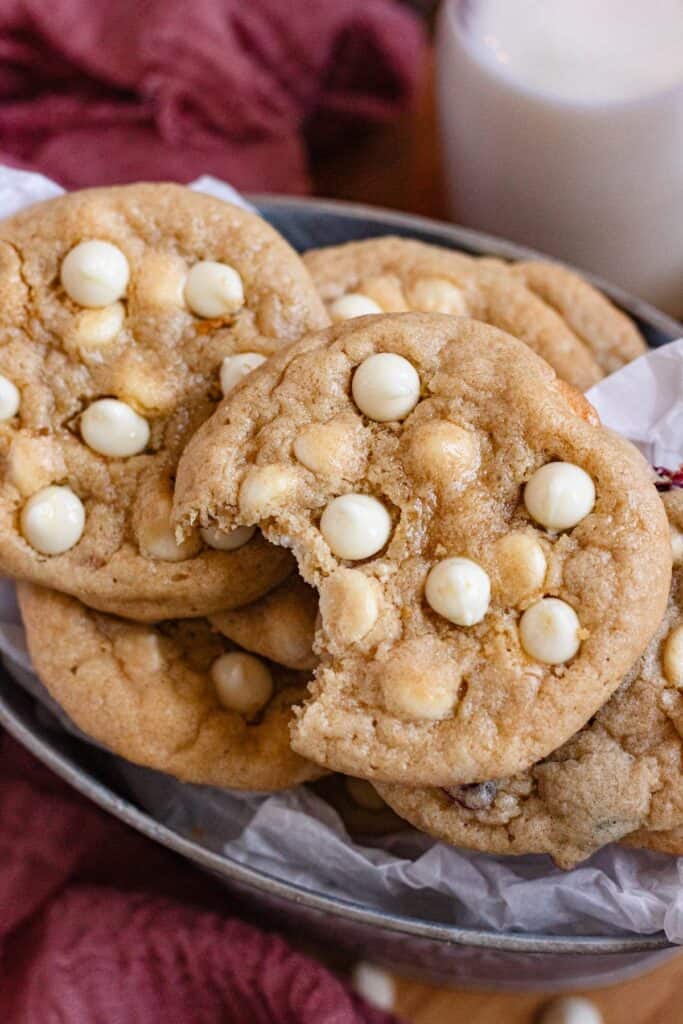 A stack of golden brown white chocolate chip cookies with a bite taken out of the top cookie.