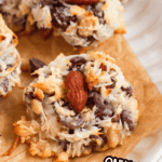 Pinterest image of a close-up shot of baked Almond Joy Cookies with coconut, chocolate chips, and whole almonds on a parchment-lined plate.