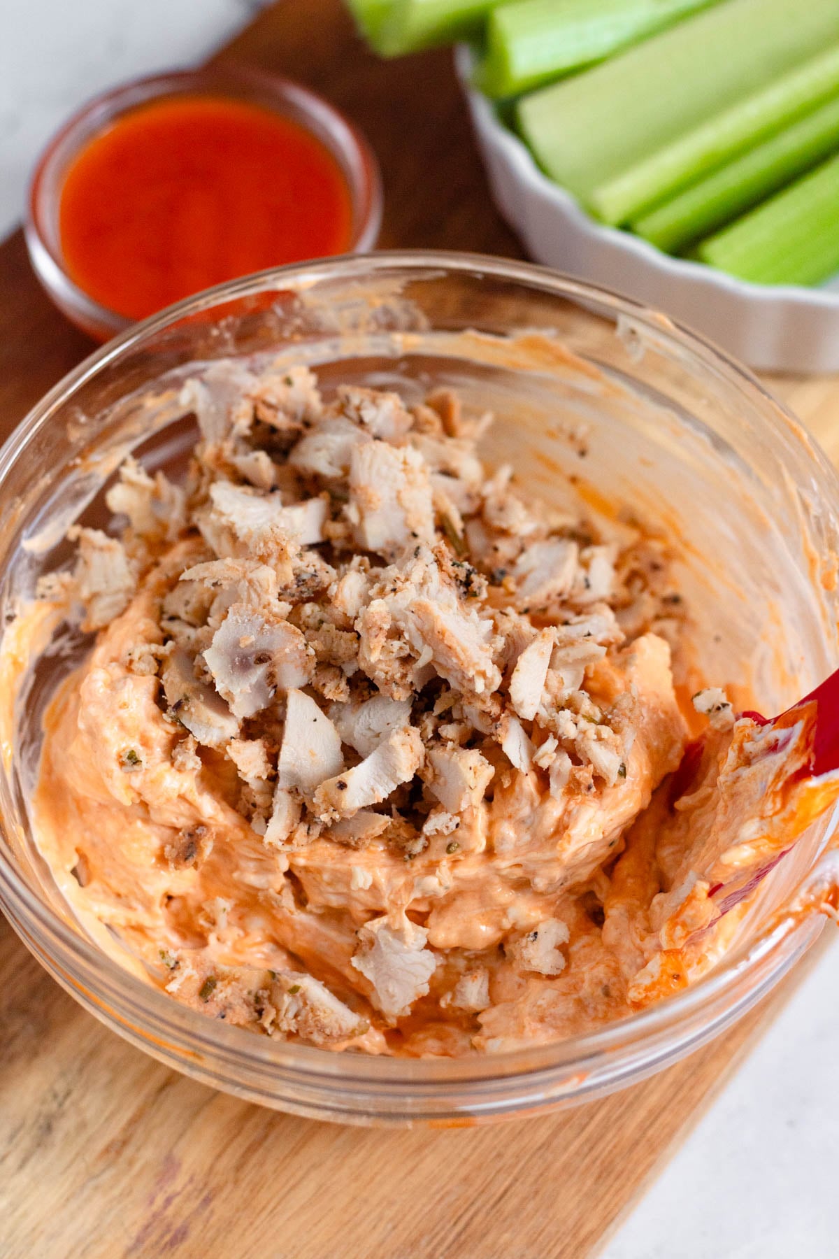 Buffalo chicken dip in a bowl with buffalo sauce and celery stalks behind it. 