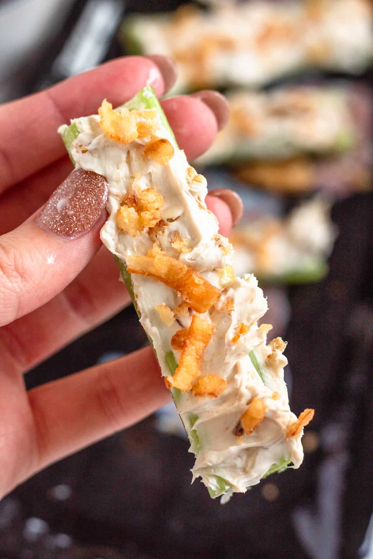 A hand holding french onion stuffed celery topped with crispy fried onions.