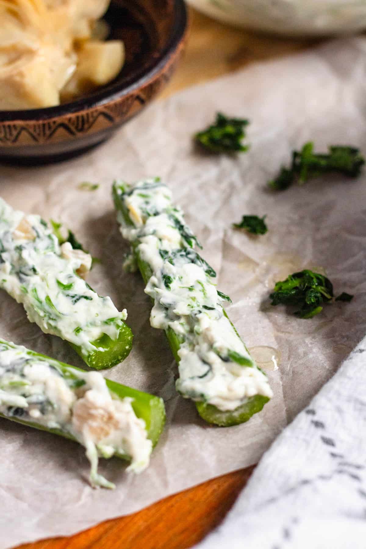 3 stalks of spinach artichoke stuffed celery on parchment paper.